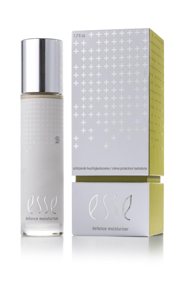 En flaska Defence Moisturiser med silverlock står bredvid en matchande vit och gul låda, båda med minimalistisk silvertext och ett plusteckensmönster.