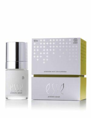 En flaska Esse Probiotic Serum med silverlock står bredvid den vitgula förpackningen med silverfärgad text och ett plusteckensmönster.