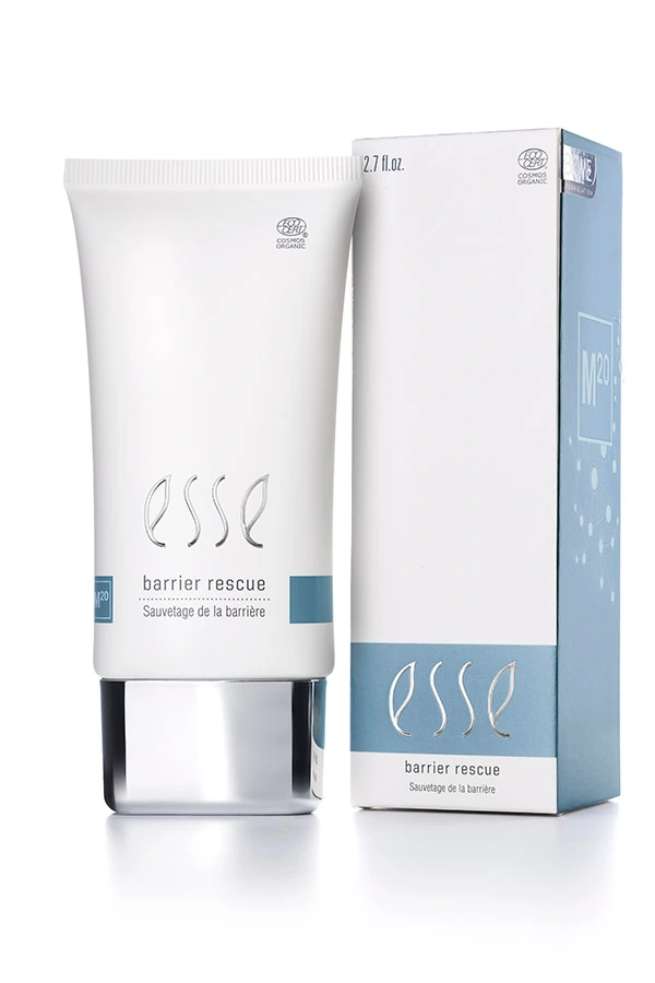 En vit tub med Esse Barrier Rescue står bredvid den tillhörande förpackningen; båda har minimalistisk text och blå detaljer. På tuben står produktnamnet ”Esse Barrier Rescue”, storleken 2,7 fl oz samt logotypen högst upp.